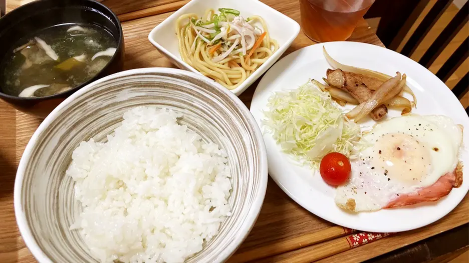 食事の例(ごはん、味噌汁、小鉢、ハムエッグ、千切りキャベツミニトマト他)